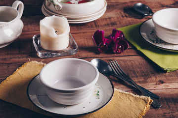Table setting with ceramic plates, bowls, cutlery, candle and orchid