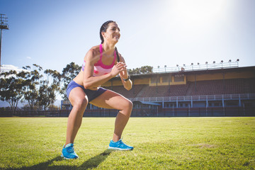 Female fitness model doing exercises outside at a sport stadium on a bright sunny day