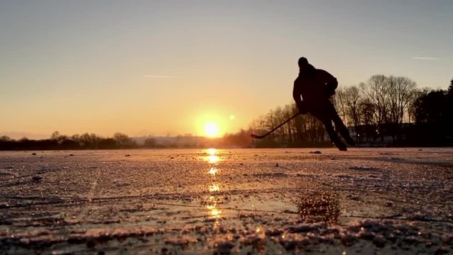 Slow-motion footage of hockey player skating on a frozen lake at sunset
