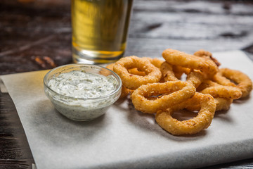 Beer of the rings of squid fried in batter with sauce on the Board for filing is covered with a sheet of parchment