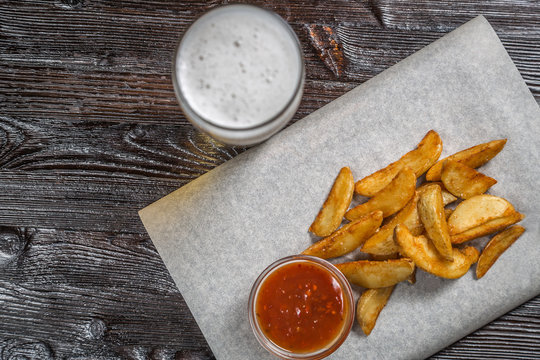 Beer snack of fried potatoes with sauce on the Board for filing is covered with a sheet of parchment. The view from the top. Copy-space. 