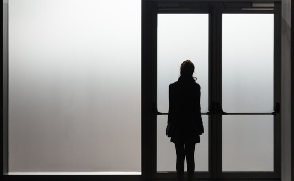 Depressed woman waiting in front a glass door in a white room ready to react - Disease - Abuse - phobia Concept.