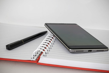 Open notebook with pen and mobile phone on it Office accessories