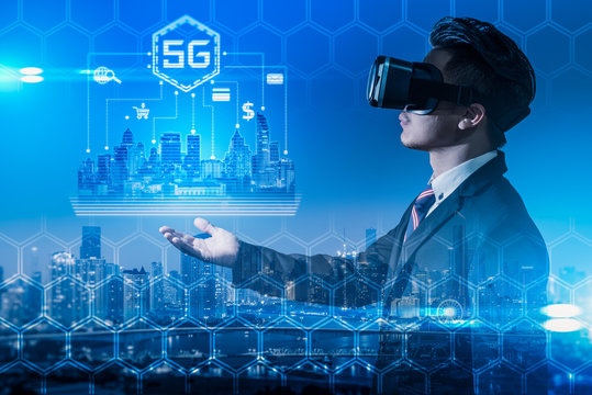 The abstract double exposure image of the business man wear a VR glasses hold the 5G hologram and cityscape is backdrop. The concept of 5G, communication, financial and internet of things.