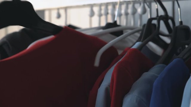 wardrobe hanger with multi-colored clothes in the store. colorful outfits hang on a hanger. a woman's hand takes a hanger with a red dress. pulls out of the closet 4k