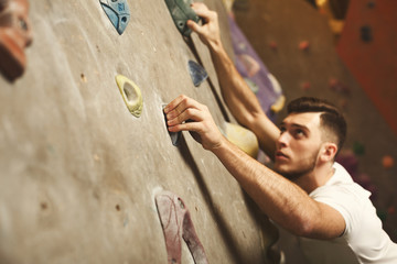 Fototapeta na wymiar Young man climbing artificial rock wall at gym