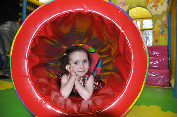 little girl playing in the nursery, laying in the soft tube in which kids love to climb like a tunnel and smiling