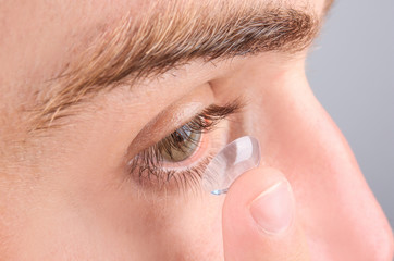 Young man putting contact lens in his eye, closeup