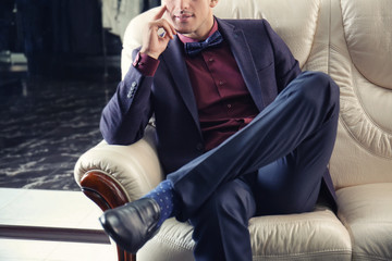 Young man in elegant suit sitting on sofa at menswear store