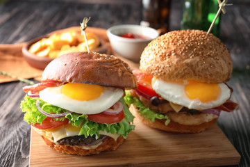 Wooden board with tasty burgers on table