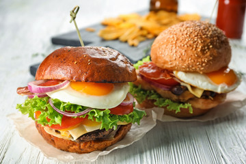 Tasty burgers with fried eggs on wooden table
