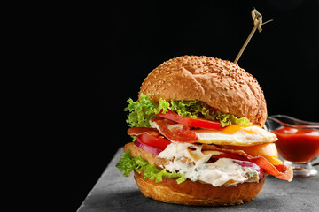 Tasty burger with fried egg on table against black background