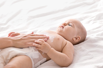 Woman applying body cream on her baby indoors