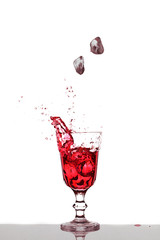 Eiswürfel fallen  in ein Glas mit rotem Getränk