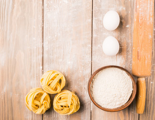 Homemade Italian tagliatelle noodles on the kitchen table and ingredients for cooking. Copy space. Flat layout