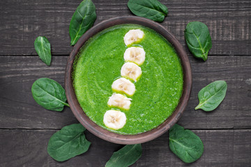 healthy green spinach smoothie bowl topped with banana on dark wooden background - obrazy, fototapety, plakaty