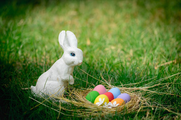 The garden decorated white rabbit with colorful easter eggs on green grass background