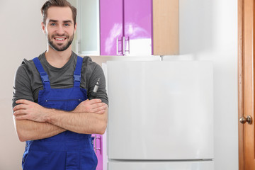 Male technician standing near modern refrigerator indoors