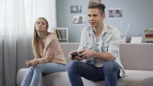 Offended girl looking at her boyfriend who indifferently playing video games