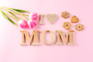 Phrase "I LOVE MOM" made of wooden letters and flowers with cookies on color background. Greetings for Mother's day