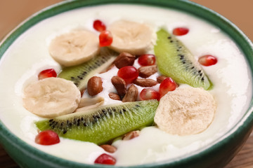 Yogurt with banana, pomegranate seeds and kiwi in dish, closeup