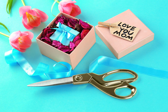 Composition with gift, flowers and scissors on color background. Greetings for Mother's day