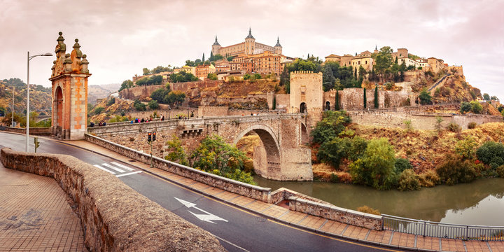 Panorama of Old city of Toledo with Alcantara Bridge across the river Tajo and Alcazar in the overcast evening, Castilla La Mancha, Spain