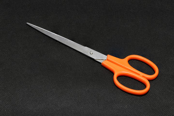 Metal scissors orange handle put on the black background. it is an instrument used for cutting, consisting of two blades laid one on top of the other and fastened in the middle.