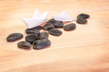 Paper Boats and Black Stones on Wood Background, Leadership concept