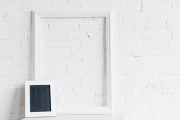 blank frame and small chalkboard in front of white brick wall, mockup concept
