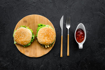 Burger on wooden cutting board on black background top view