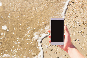 A woman is holding a phone against a sea beach. Blank screen