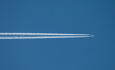 Airplane flying at high altitude leaving its white wake over blue sky