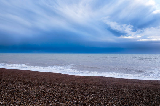 Brighton beach, Sussex, Ubited Kingdom, at the bottom a line of red pebble beach in the middle the sea and at the top of the image a deep blue and white dramatic stormy sky