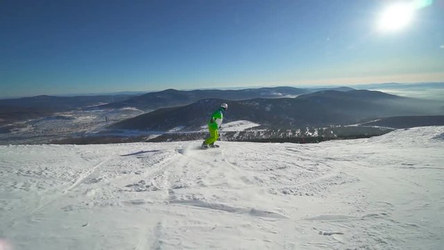Sportsman in bright green clothes jumps on snowboard upon a slope of the hill at sunny winter day