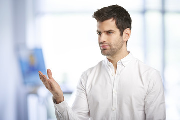 Portrait of smiling young businessman pointing something with his finger while standing at the office and looking at camera