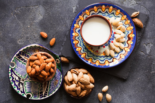 Almond milk in a clay pot and fresh nuts over dark slate background, selective focus. Dairy-free, vegan healthy food concept