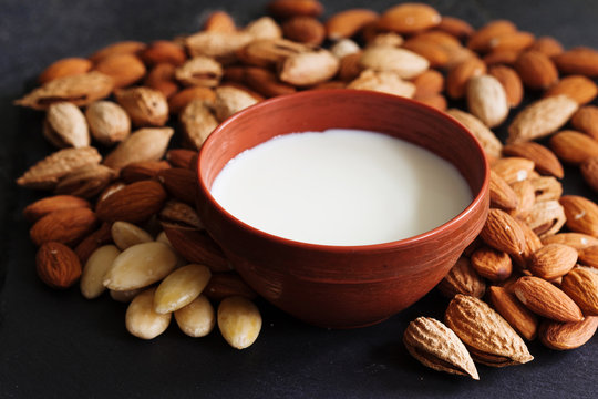 Almond milk in a clay pot and fresh nuts over dark slate background, selective focus. Dairy-free, vegan healthy food concept