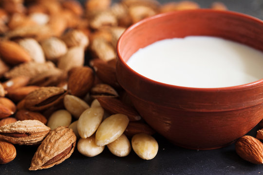 Almond milk in a clay pot and fresh nuts over dark slate background, selective focus. Dairy-free, vegan healthy food concept