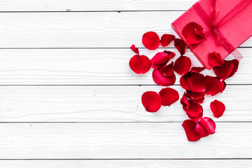 Gift for Valentine's day. Red gift box near red rose petals on white wooden background top view copy space