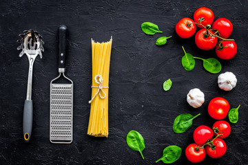 Italian pasta concept. Spaghetti, tomatoes, garlic, cheese grater, spoon for spaghetti on black background top view
