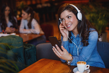 Young woman listening to music via headphones and smartphone in a cafe