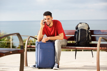 Fototapeta premium happy male traveler sitting on bench with bags and talking on mobile phone