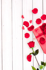 Prepare the prsesnts or surprise for Valentine's day. Red gift box near red rose and petals on white wooden background top view space for text