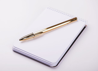 Notepad with blank paper next to golden ball pen on white background. Isolated. Mockup.