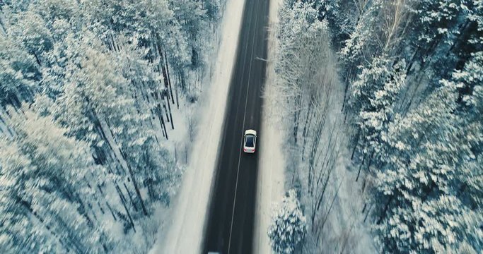 A car moves on a two lane winter road in a forest.