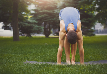 Sporty man doing Standing Forward Bend outdoors