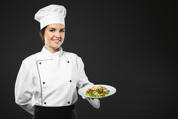 Portrait of female chef with tasty salad on black background