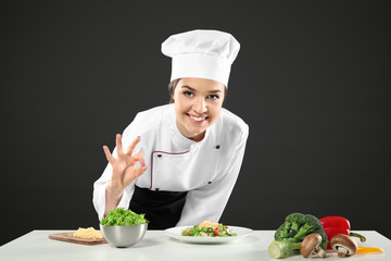Female chef near table with products against black background