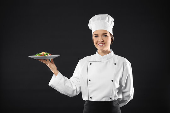 Portrait of female chef with tasty salad on black background